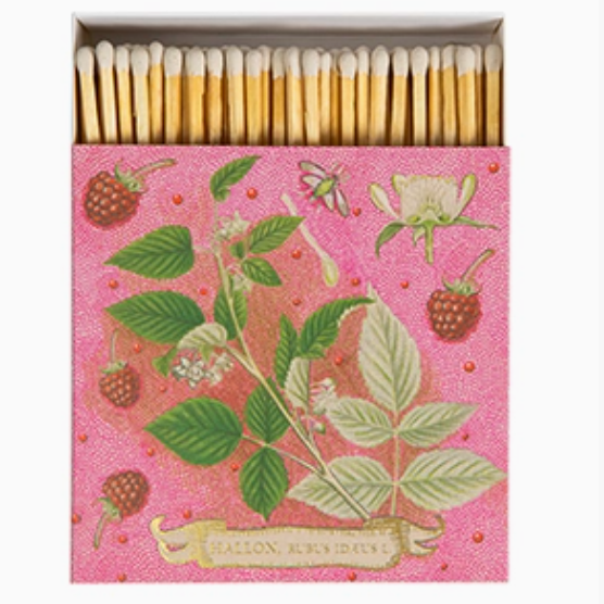 A decorative matchbox filled with wooden matches. The matchbox lid is pink with botanical illustrations of green leaves, raspberries, and a white flower, plus a small dragonfly.