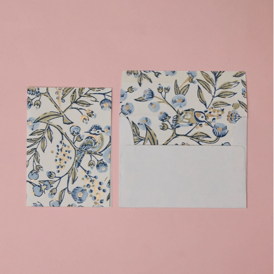 A floral and bird patterned stationery set featuring a small rectangular card and a matching envelope with a white blank writing area, displayed on a solid pink background.