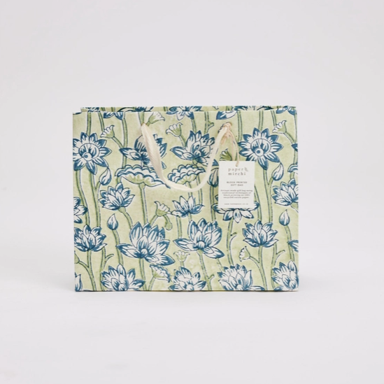 A rectangular gift bag with a light green background and a blue floral pattern, featuring cream-colored paper handles and a small white hanging label. The brand name 'BUTTERFLY HOUSE' is visible on the label.
