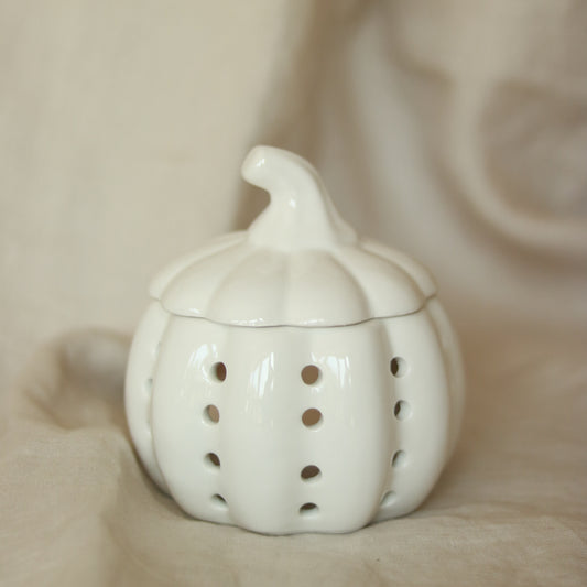 White ceramic pumpkin-shaped wax melt burner with pierced dot detail and removable lid styled on a cream linen background