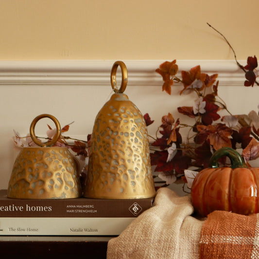 Decorative Bronze Metal Bells in large and small sizes styled on stacked books with autumn leaves and a glazed pumpkin ornament — rustic autumn home decor by The Rustic Barn Company