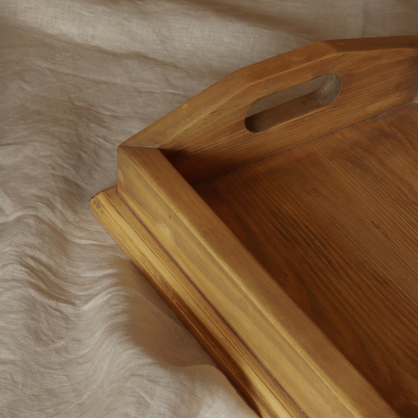 Close-up of Manor handcrafted wooden tray showing cut-out handle and natural wood grain detail on soft linen