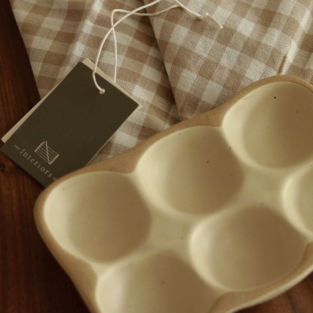 Overhead close-up of the empty stoneware egg tray beside a checked cloth and product tag