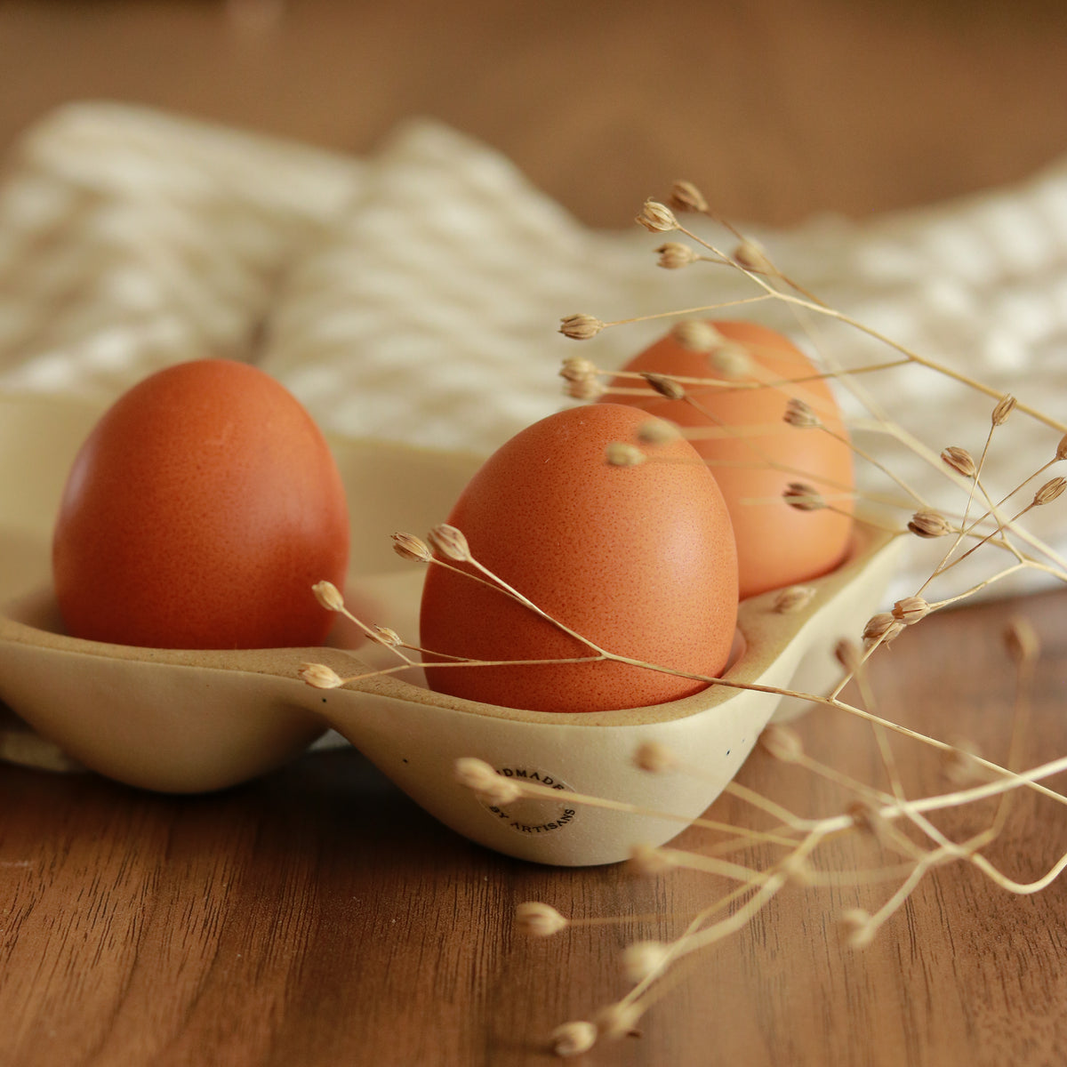 Three brown eggs in a Weathered Oat stoneware egg tray on a wooden table