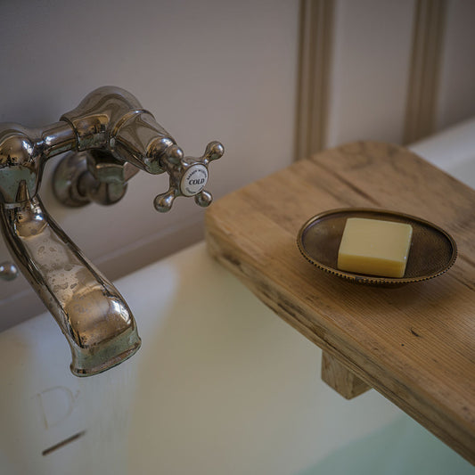 Vintage-style faucet with a soap dish holding a bar of soap on a wooden shelf.