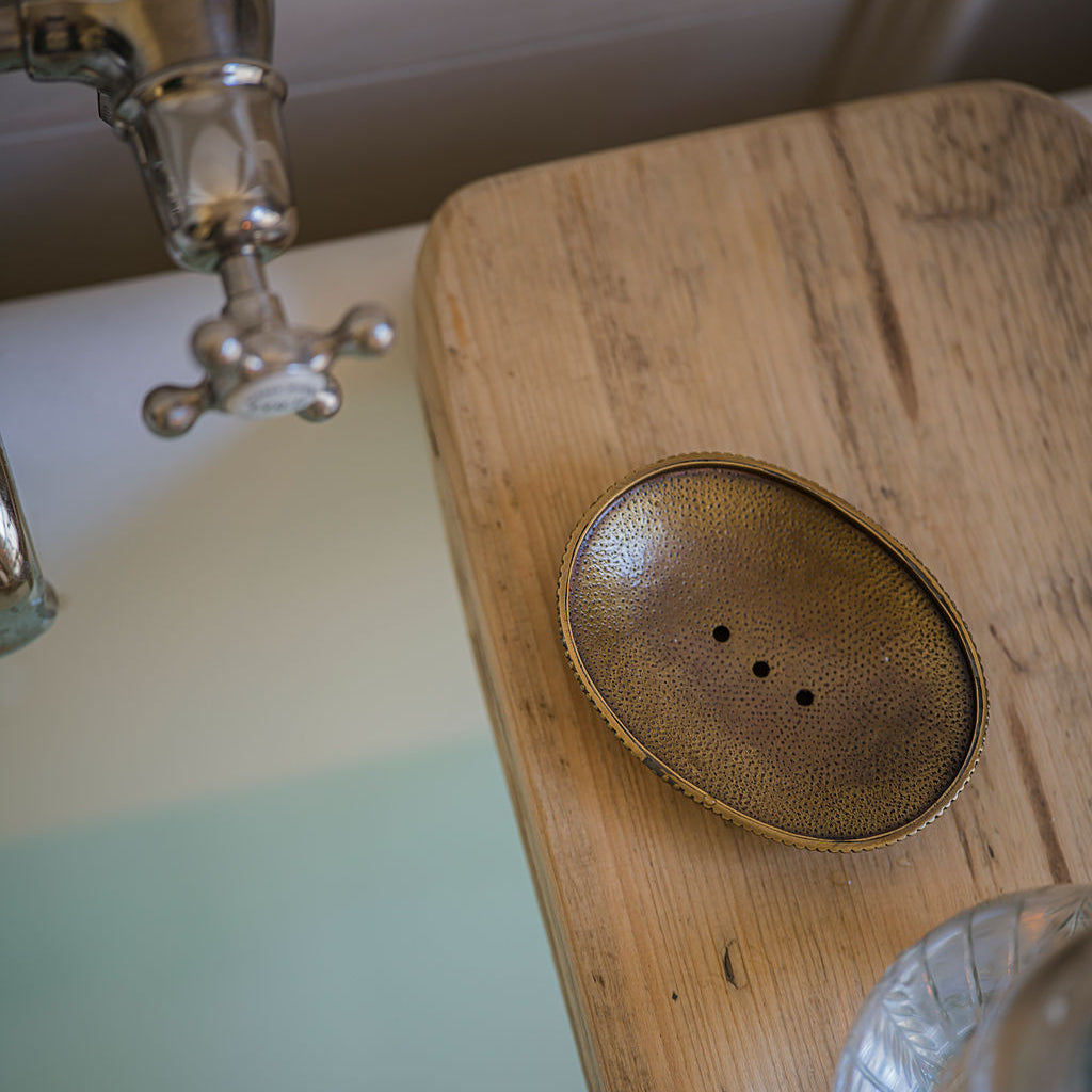 Bronze soap dish on a wooden surface with a vintage-style faucet in the background.