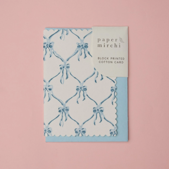 A Paper Mirchi block printed cotton card featuring a light blue and white pattern, displayed on a solid pink background.