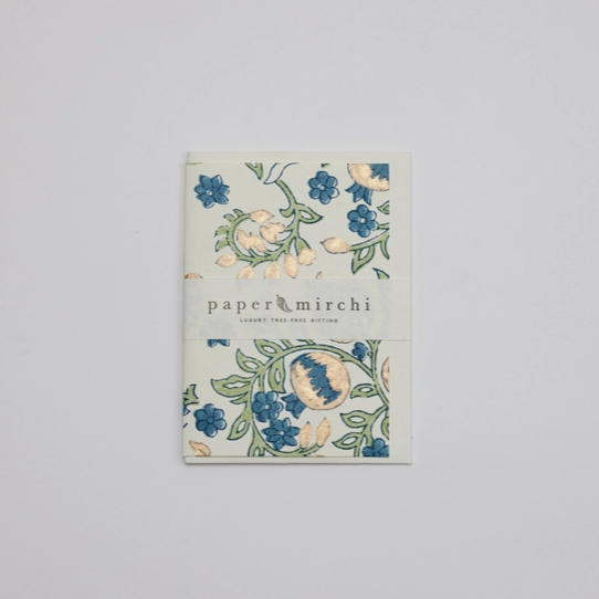 A folded sheet of Paper Mirchi Indian Fine Art Paper with a botanical floral pattern in blue, green, and beige, displayed on a neutral light gray background.