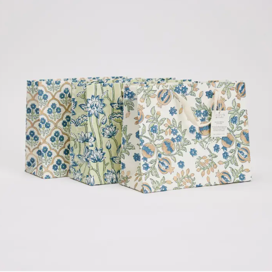 Three decorative gift bags with floral and geometric patterns in blue, green, and beige, arranged side-by-side on a light gray background.