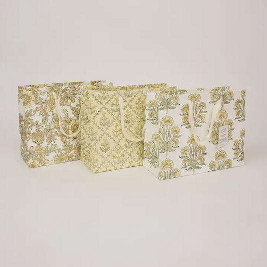 Three decorative paper shopping bags with cream handles, featuring botanical and damask patterns in muted olive green and beige, arranged against a plain light gray background.