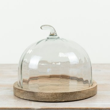 Pumpkin-shaped clear glass dome cake plate with ridged body and curved handle on a round natural wood base against a white background