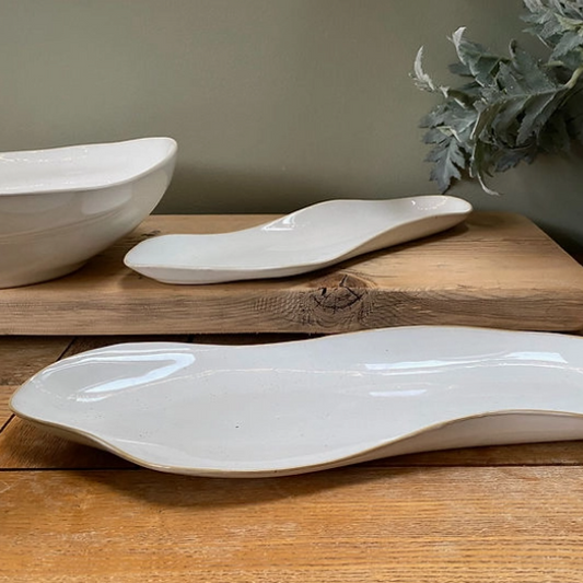 Set of 2 Dune white reactive glaze canape serving platters in large and small sizes, styled on a solid oak chopping board on a rustic wood table with a eucalyptus plant and sage green wall behind
