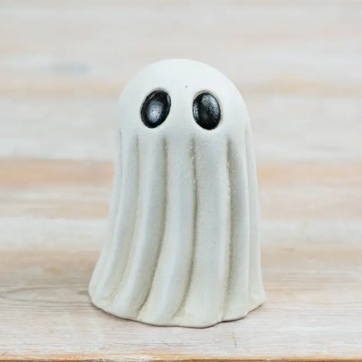 A small ghost-shaped ceramic figurine with black eyes, standing on a light wood surface.