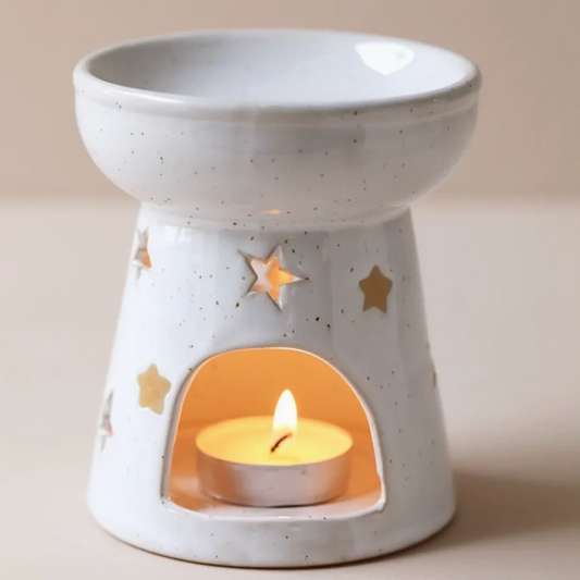 Speckled white ceramic star wax melt burner with bowl dish on top and star cutouts, lit tealight glowing inside, on a neutral background