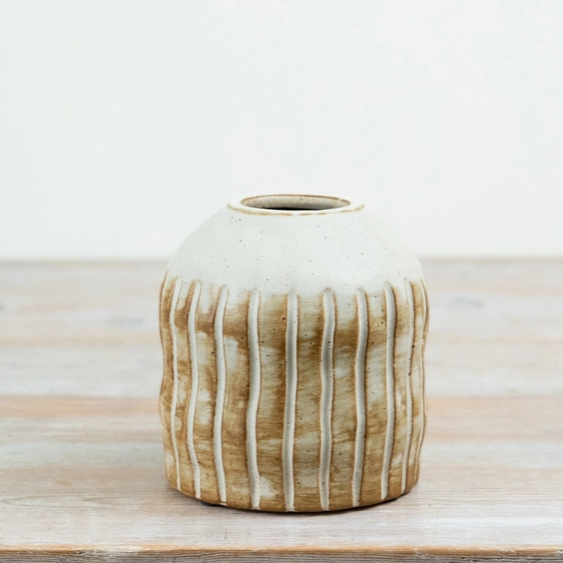Natural ribbed ceramic vase viewed from a slight angle, showing the vertical ribbing and narrow opening at the top