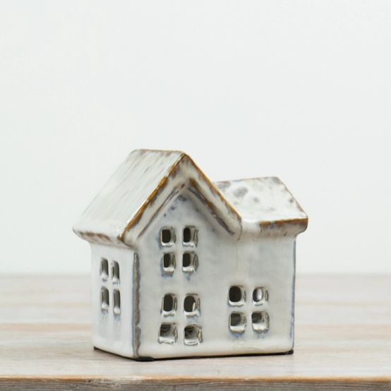 Neutral ceramic house tealight holder with a multi-gabled roof and cut-out windows, angled view