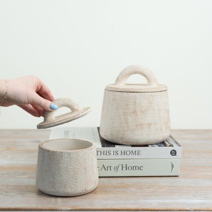 Two cement storage pots styled on books, with a hand lifting the arched lid to show the storage inside