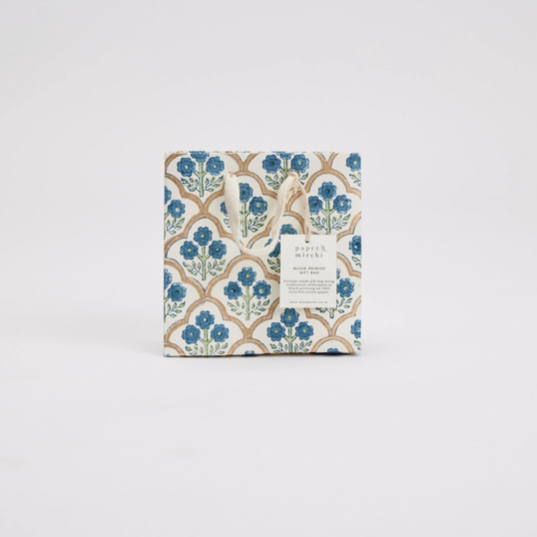 A square fabric or paper product with a repeating blue floral and tan geometric pattern, shown in its packaging with a small white label on a plain light gray background.