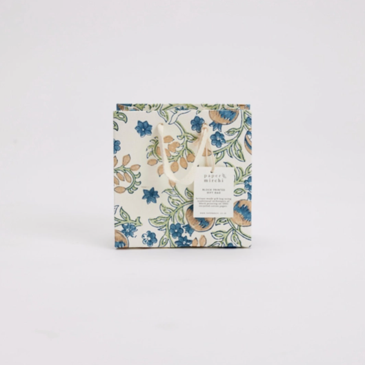 A square gift box with a delicate floral pattern in blue, green, and beige on an off-white background, featuring a white paper label on the front, set against a plain light gray background.