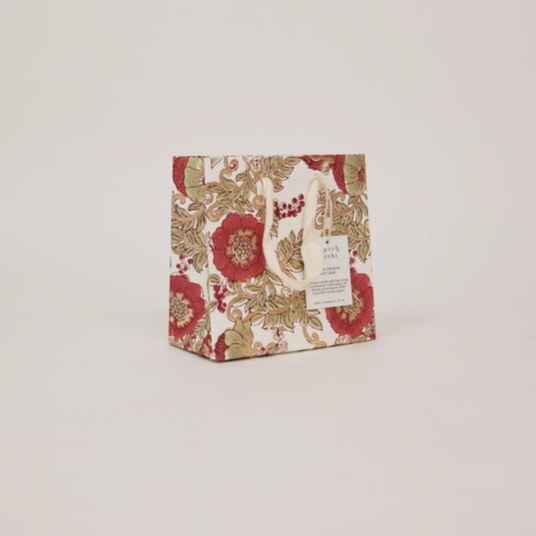 A small gift bag with a vintage floral pattern in red, gold, and cream, featuring a white paper hangtag, set against a solid light gray background.